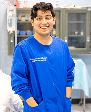 A person wearing a blue scrub top labeled "安诺卡技术学院 外科手术技术" smiles broadly in a clinical laboratory setting.